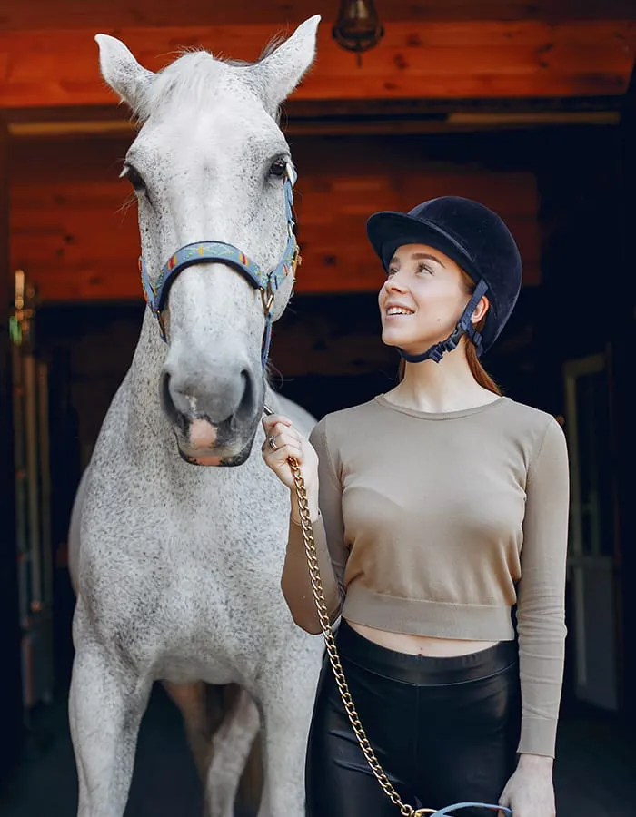 Amazzone accanto a un cavallo grigio in scuderia